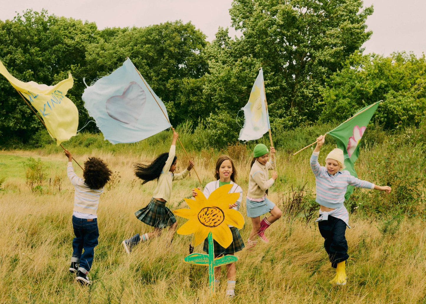 Group of children running in a grassy field holding colorful flags and wearing casual playful outfits