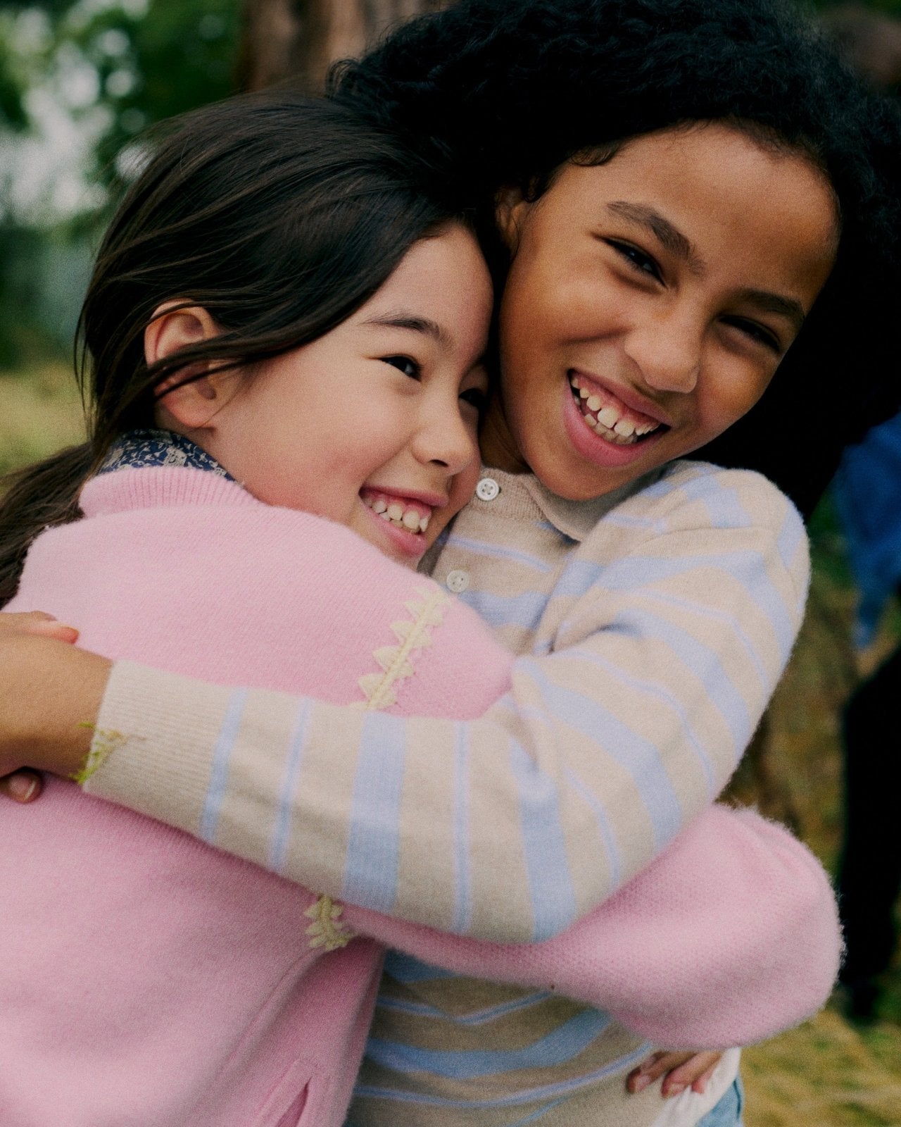 Two smiling children hugging outdoors, wearing soft pastel sweaters with subtle knit details, cozy and warm look
