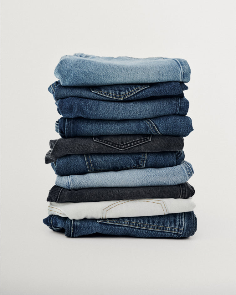 Stack of folded denim jeans in various shades of blue and black arranged neatly against a light gray background