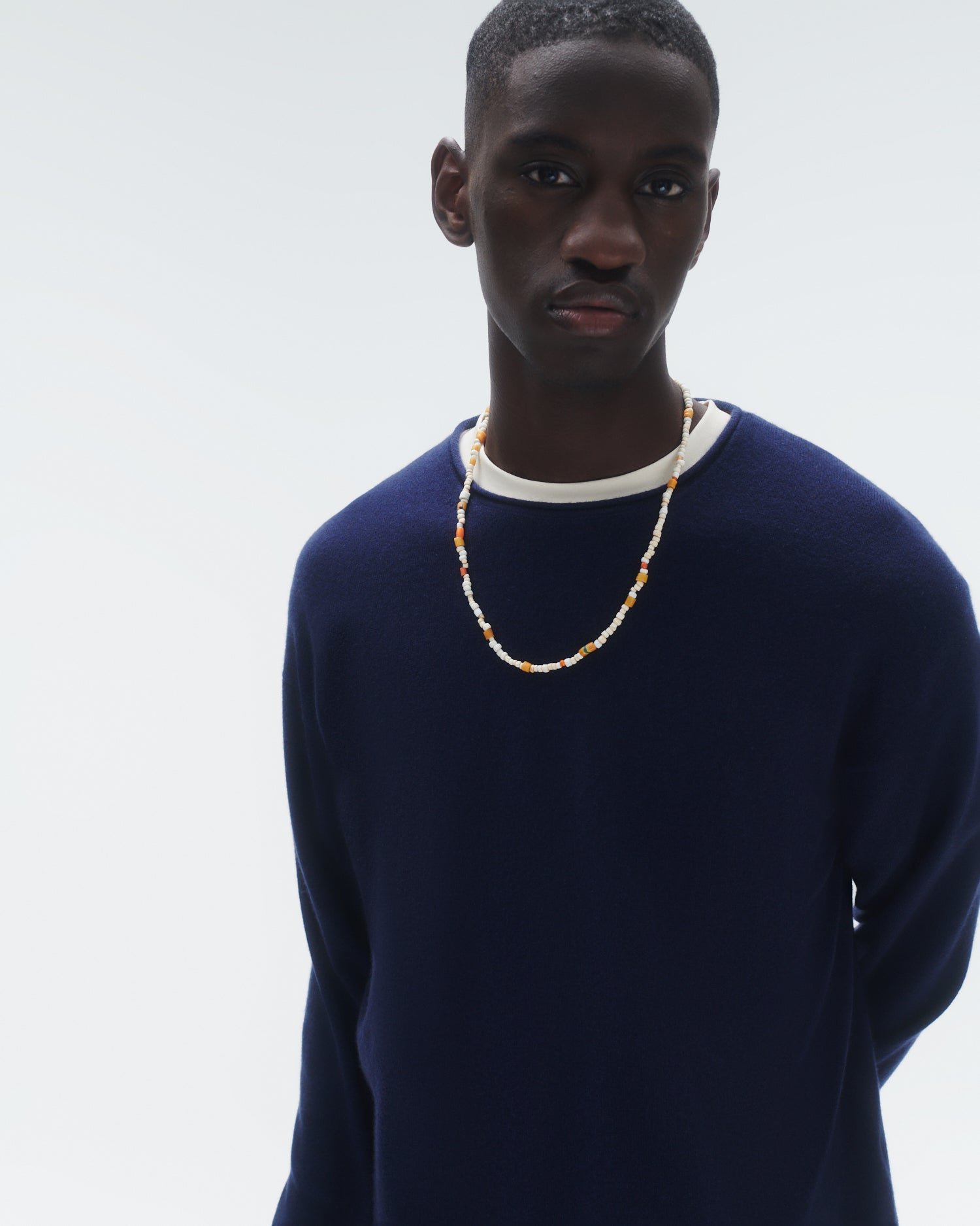 Close up of made model wearing a navy cashmere oversized crew layered over a white t-shirt and topped with a white and yellow necklace
