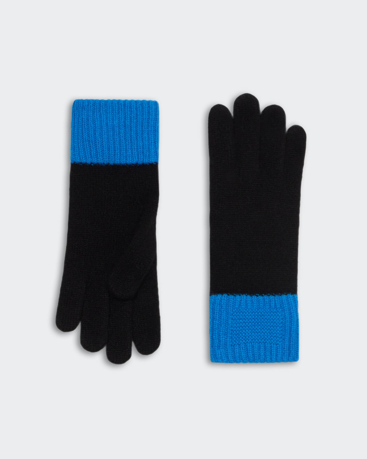Black knit gloves with bright blue cuffs laid flat on a gray background for winter wear