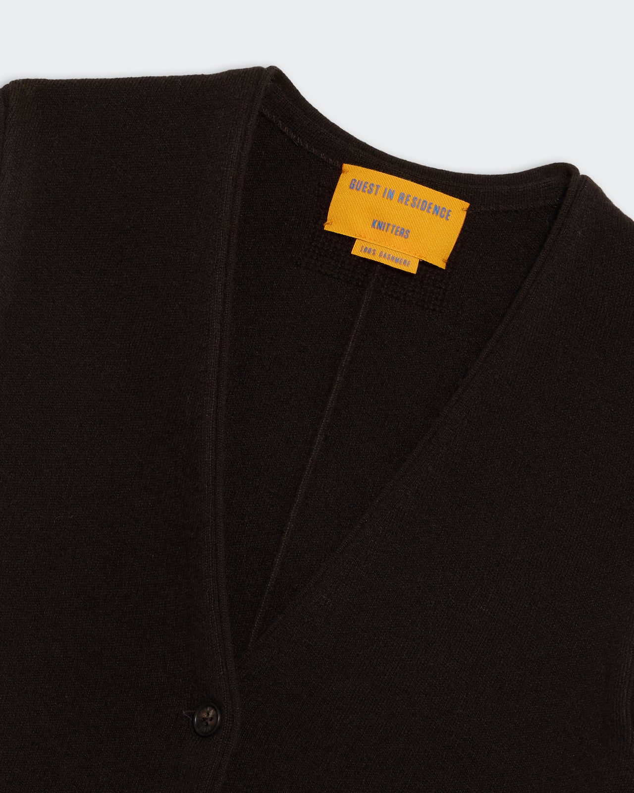 Tailored Vest - Burnt Cocoa close-up of black knitted fabric with yellow label and button detail on collar area