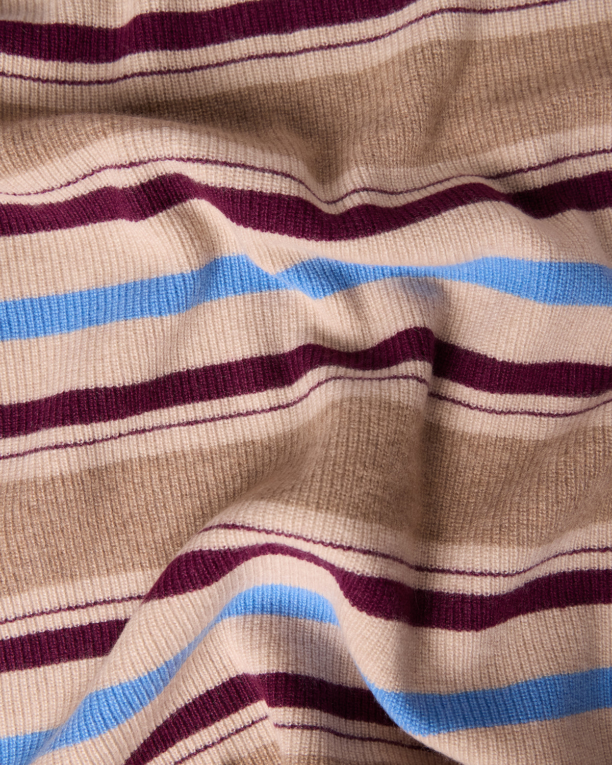 Close-up of a soft, textured fabric in beige with blue and burgundy stripes, showcasing the detailed knit of the Striped Blanket - Sandstone Combo.