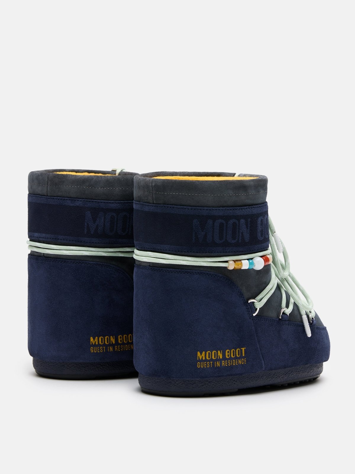 Pair of navy blue MB X GIR ICON low suede Moon Boots with decorative beads and soft lining shown from rear angle