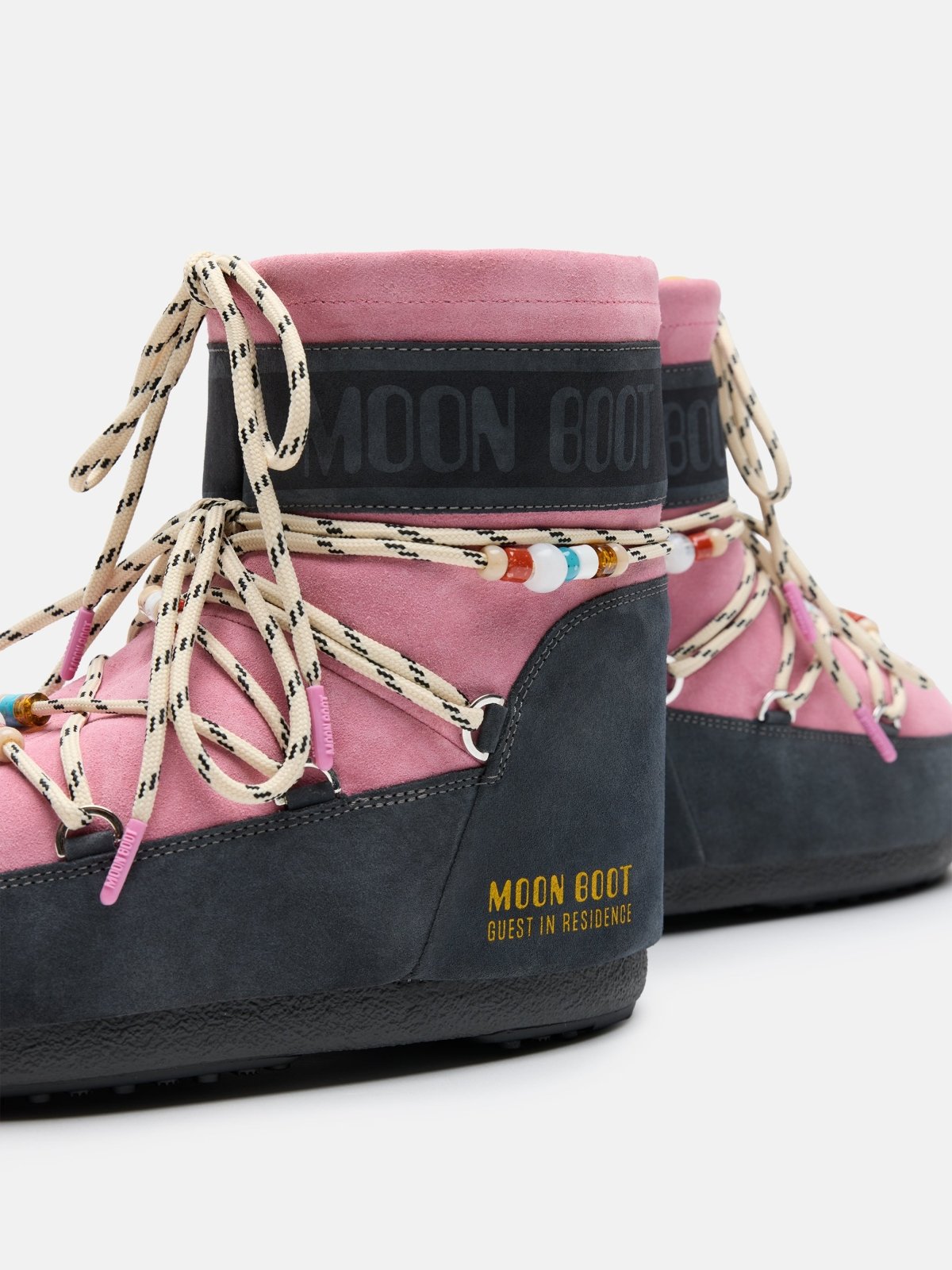 Pair of pink and grey suede Moon Boot sneakers with beige laces and beaded details, gender-neutral design.