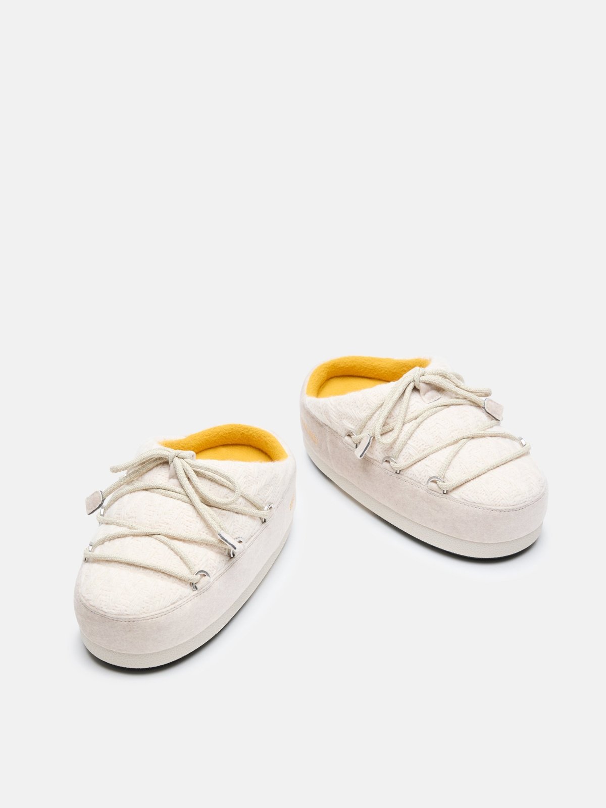 Pair of white knit mule slippers with beige laces and soft yellow interior lining on a white background