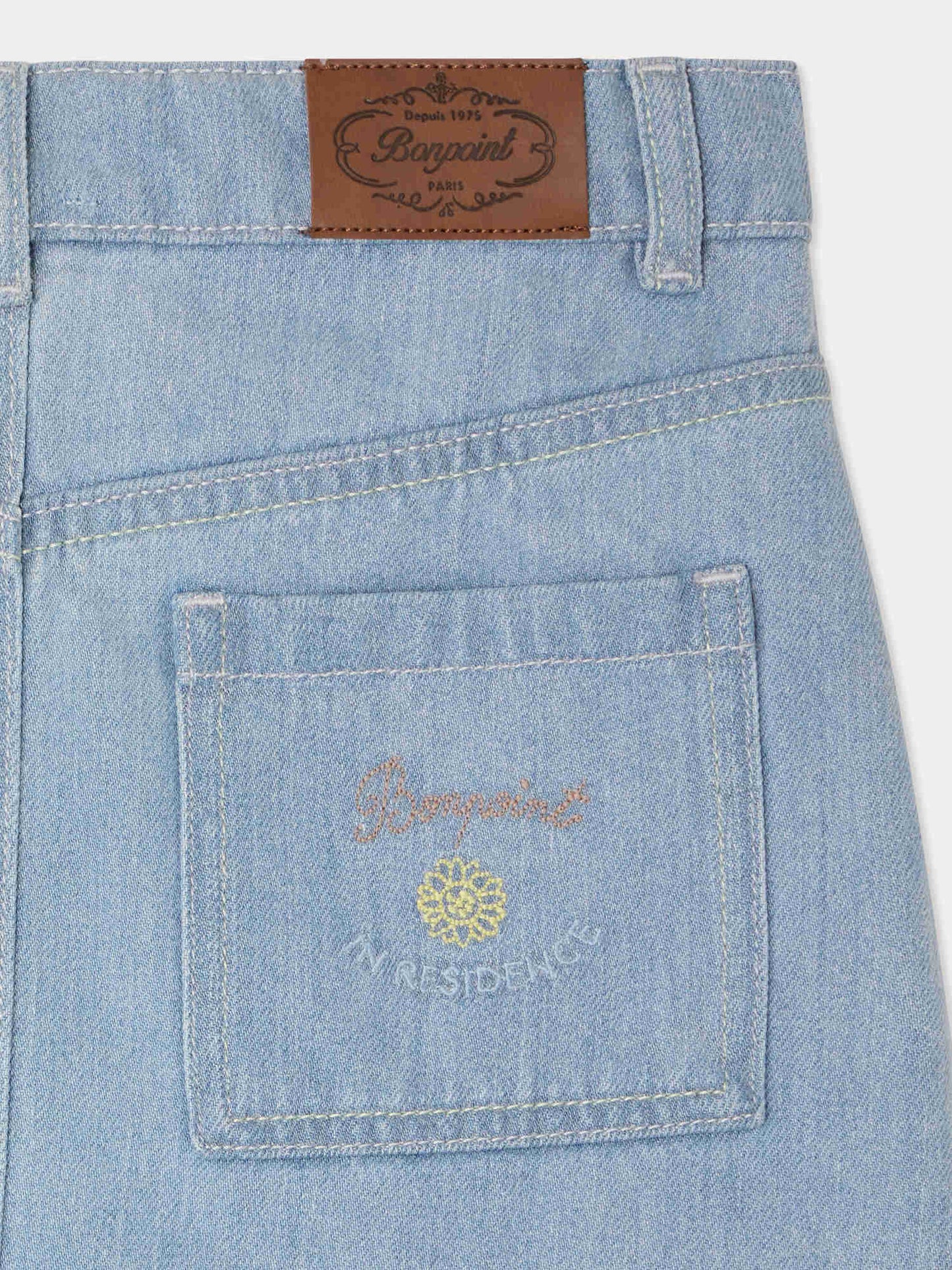 Close-up of light blue cotton denim skirt pocket with embroidery and leather brand patch on waistband