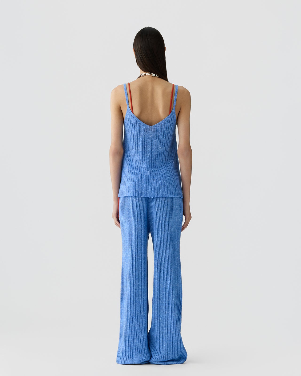 Person standing facing away wearing a blue ribbed sleeveless top with double straps and matching wide-leg ribbed pants against a plain light background