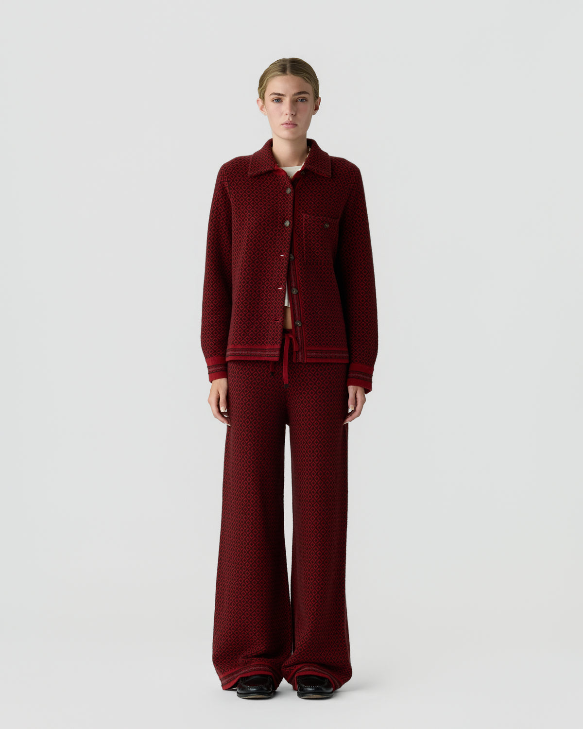 A woman stands against a plain light gray background wearing a matching dark red textured knit jacket with buttons and wide-leg pants, paired with black shoes.
