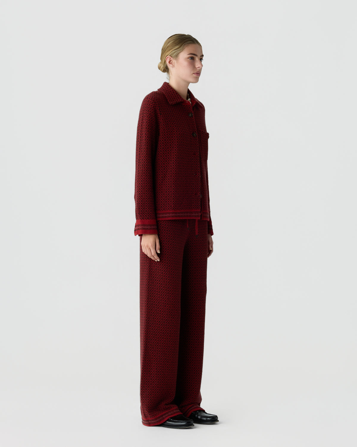 Side view of a woman wearing a matching deep red textured knit jacket and wide-leg pants with black shoes, standing against a plain light background.
