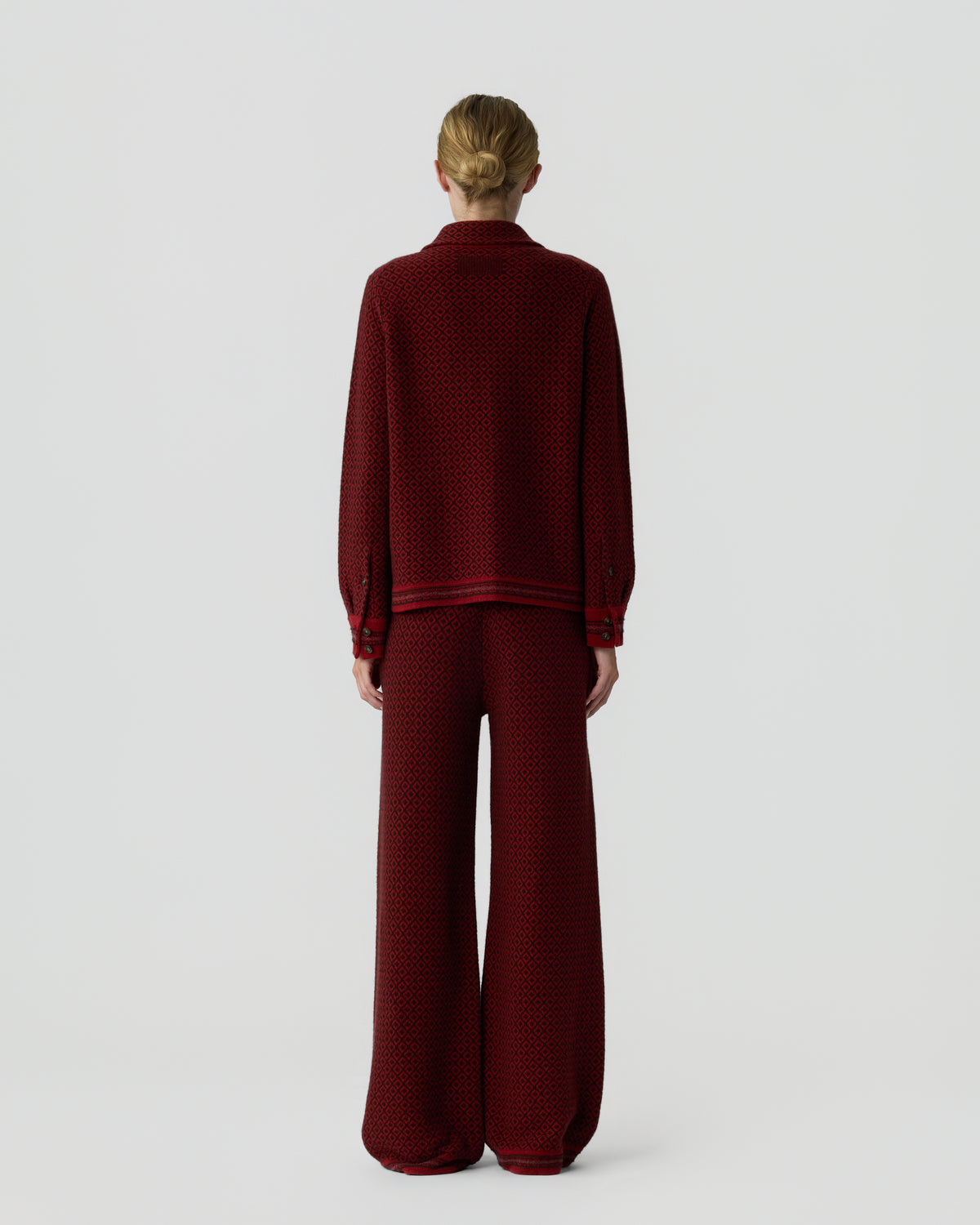 Woman standing facing away wearing a matching dark red long-sleeve top and wide-leg trousers with a subtle pattern against a plain light background.