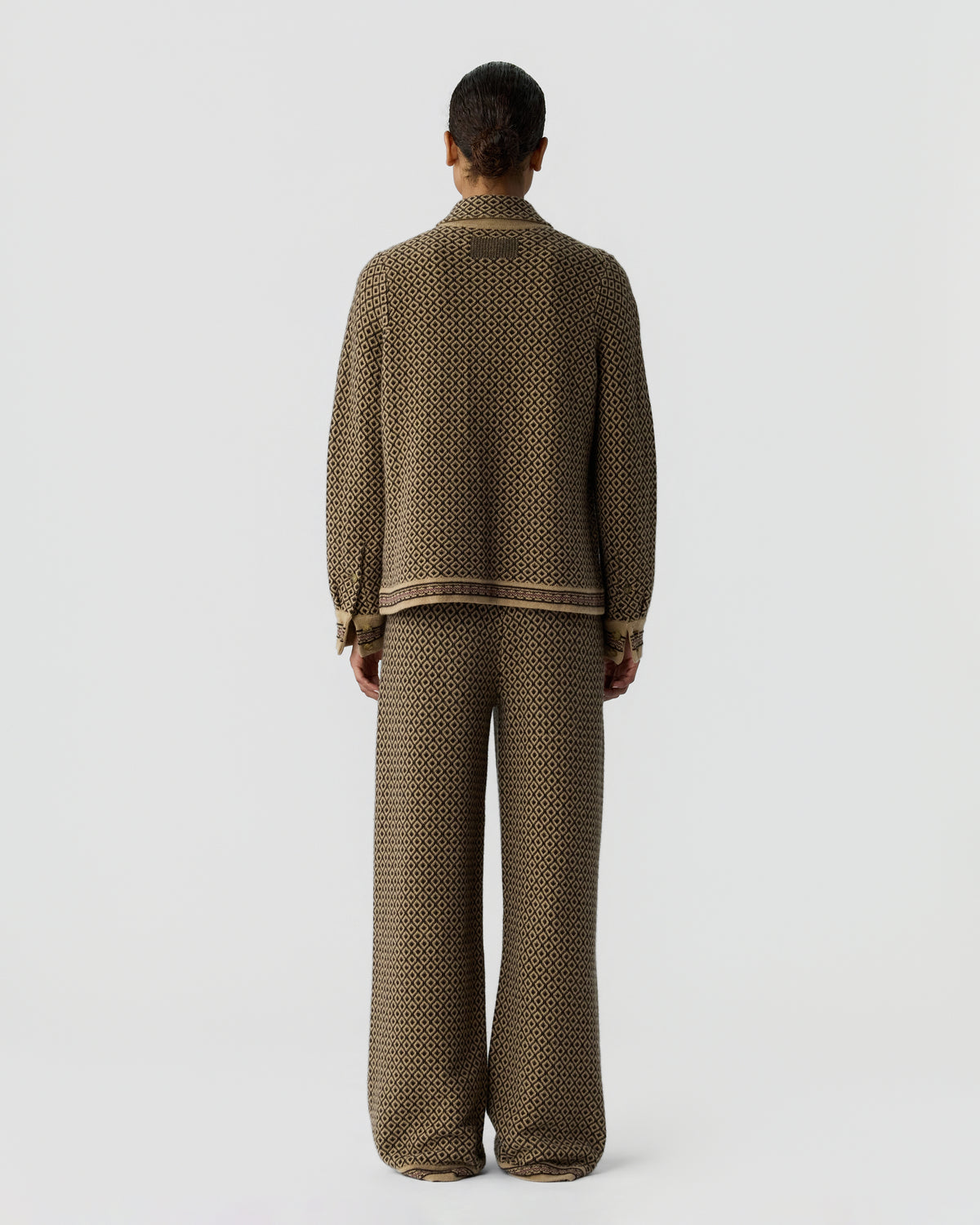 Rear view of a model wearing a brown patterned knit cardigan and matching wide leg trousers against a light gray background
