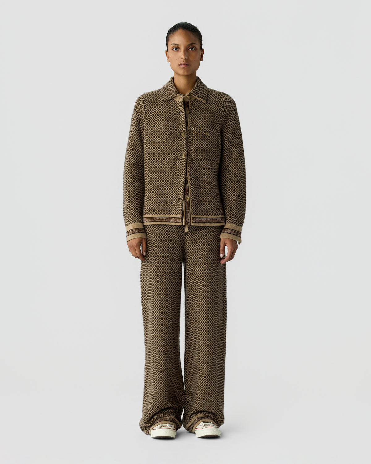Woman wearing a brown textured knit cardigan with matching wide leg trousers and white sneakers against a light gray studio background