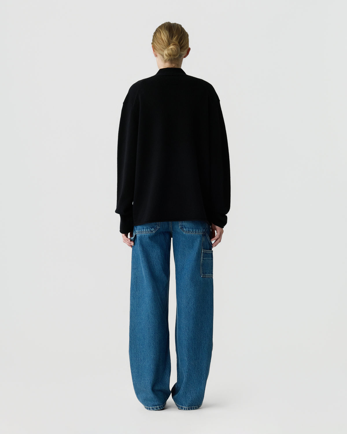 Rear view of a person wearing a black long sleeve sweater and relaxed blue jeans with a side utility pocket