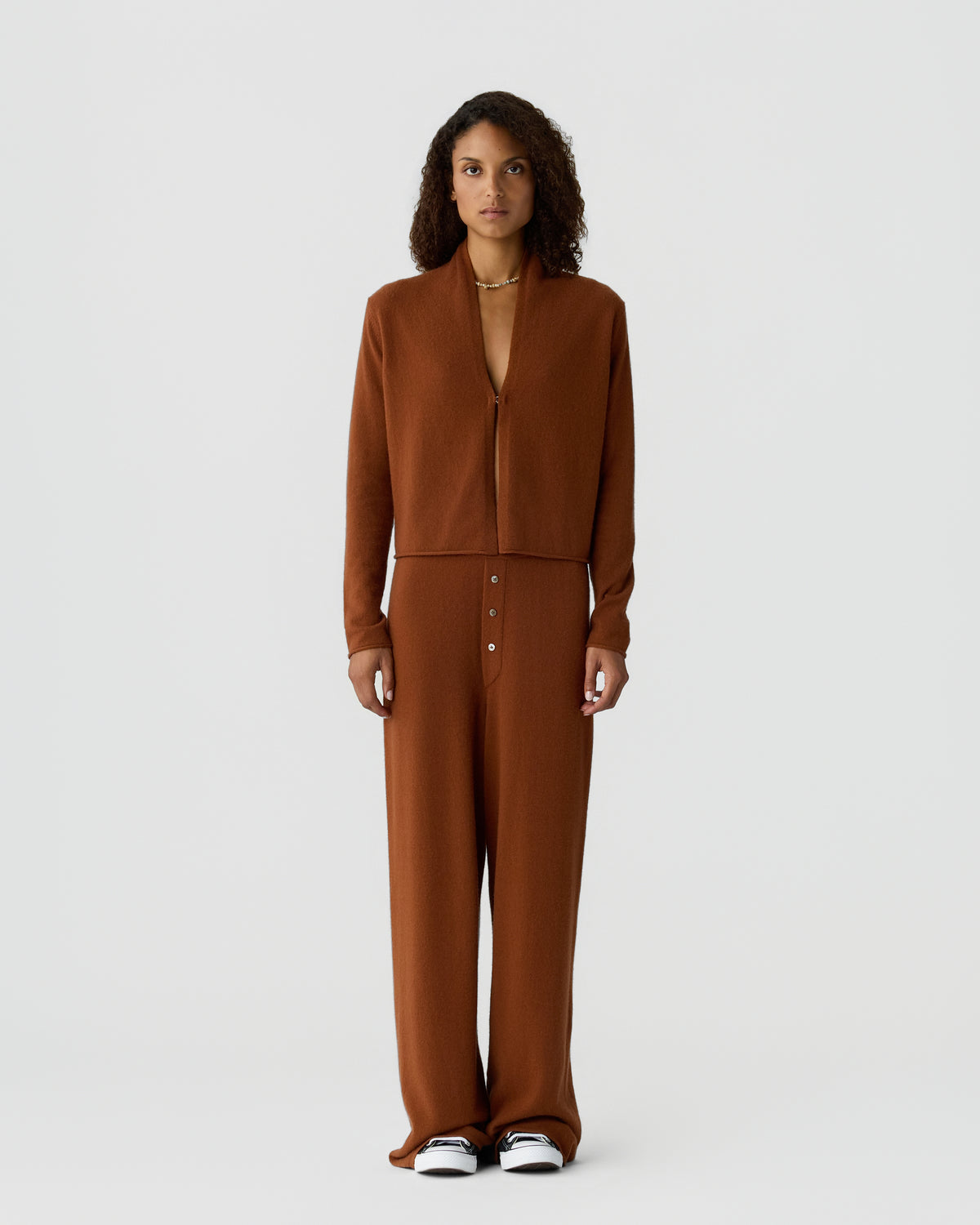 Woman wearing a brown cashmere zip front top with matching wide leg trousers and white sneakers against a light gray background