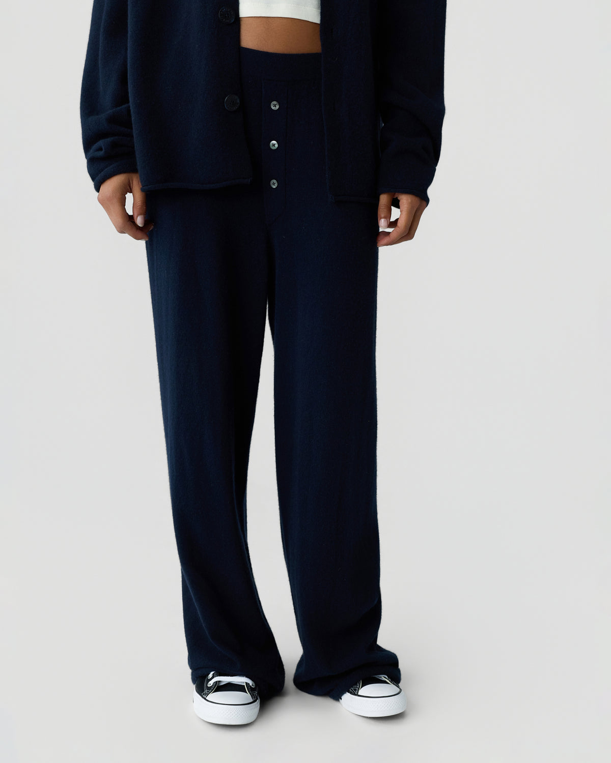 Cropped view of a person wearing a dark navy cardigan and matching wide leg trousers with a white crop top and white low top sneakers