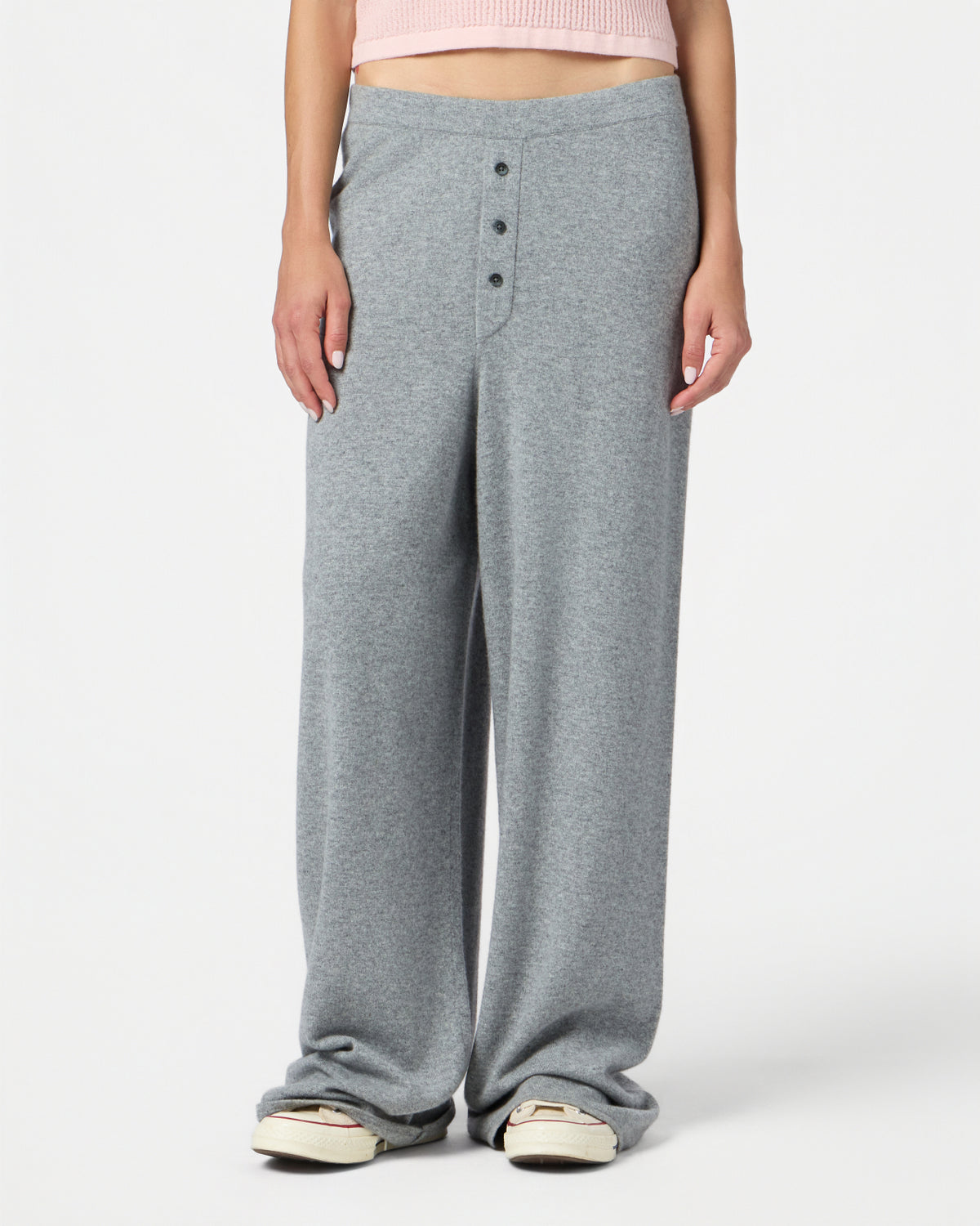 Person wearing loose heather grey wide-leg pants with a three-button front detail, standing with feet slightly apart and white sneakers visible beneath the hem.