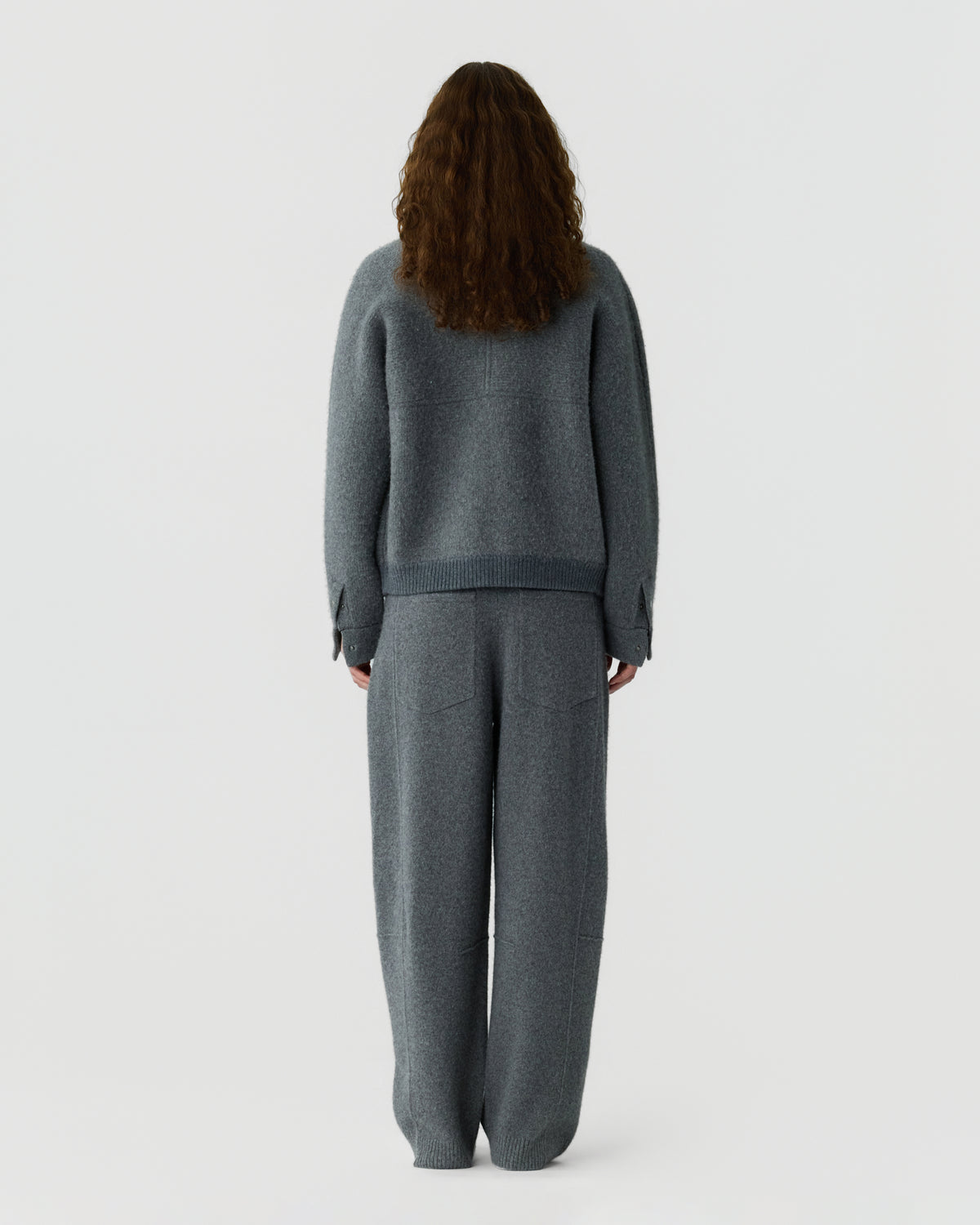 Rear view of a person wearing a charcoal gray knit sweater and matching relaxed trousers against a plain light background