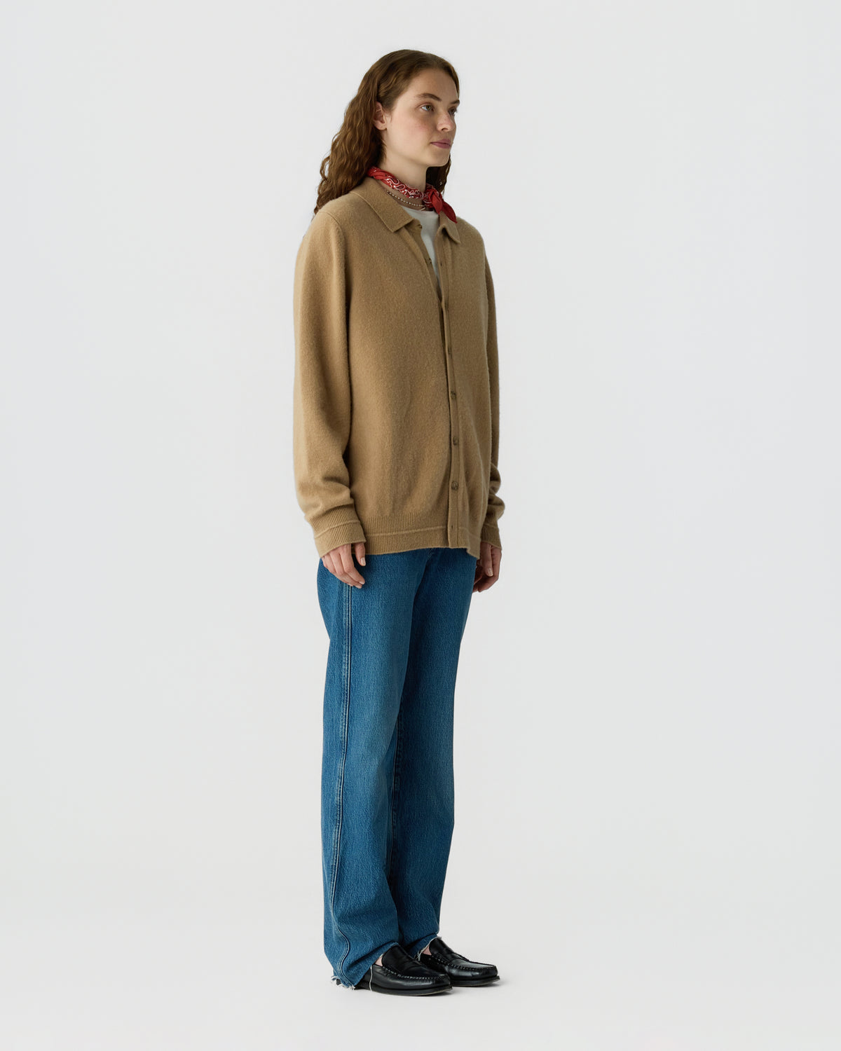 Woman standing in a tan zip front sweater with blue jeans and black shoes against a light gray studio background