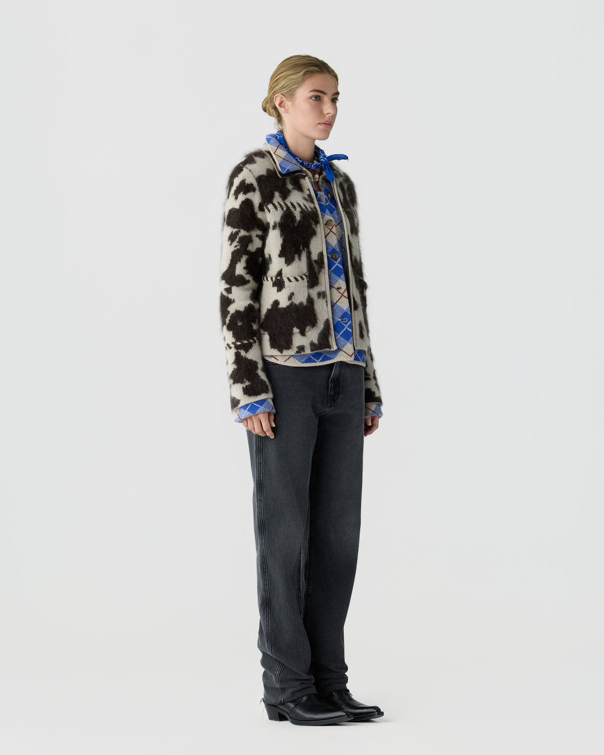Model wearing a black and white patterned cardigan over a blue patterned top with dark trousers and black shoes against a light gray background
