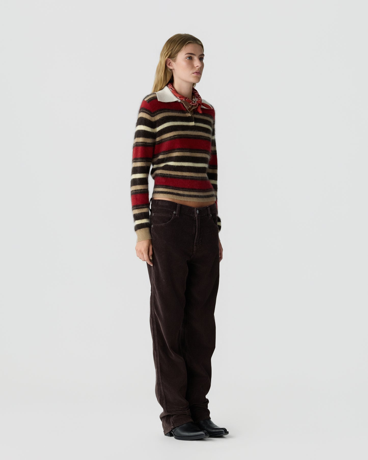 Woman wearing a striped long-sleeve sweater with red, brown, and beige colors, paired with dark brown wide-leg pants and black shoes, standing against a plain background.