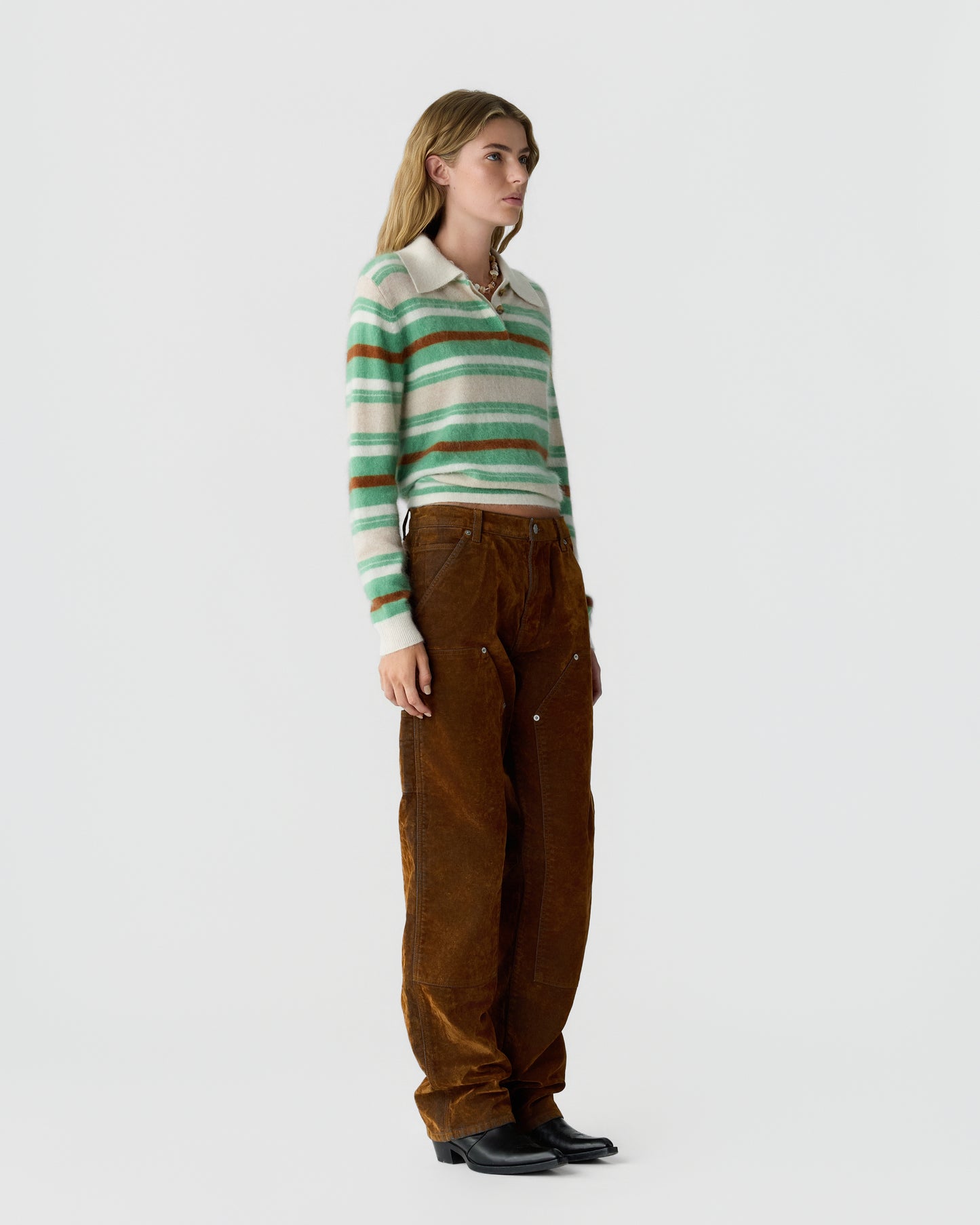 Woman standing wearing a striped green and beige long sleeve sweater with a collar, brown corduroy pants, and black boots against a plain white background.