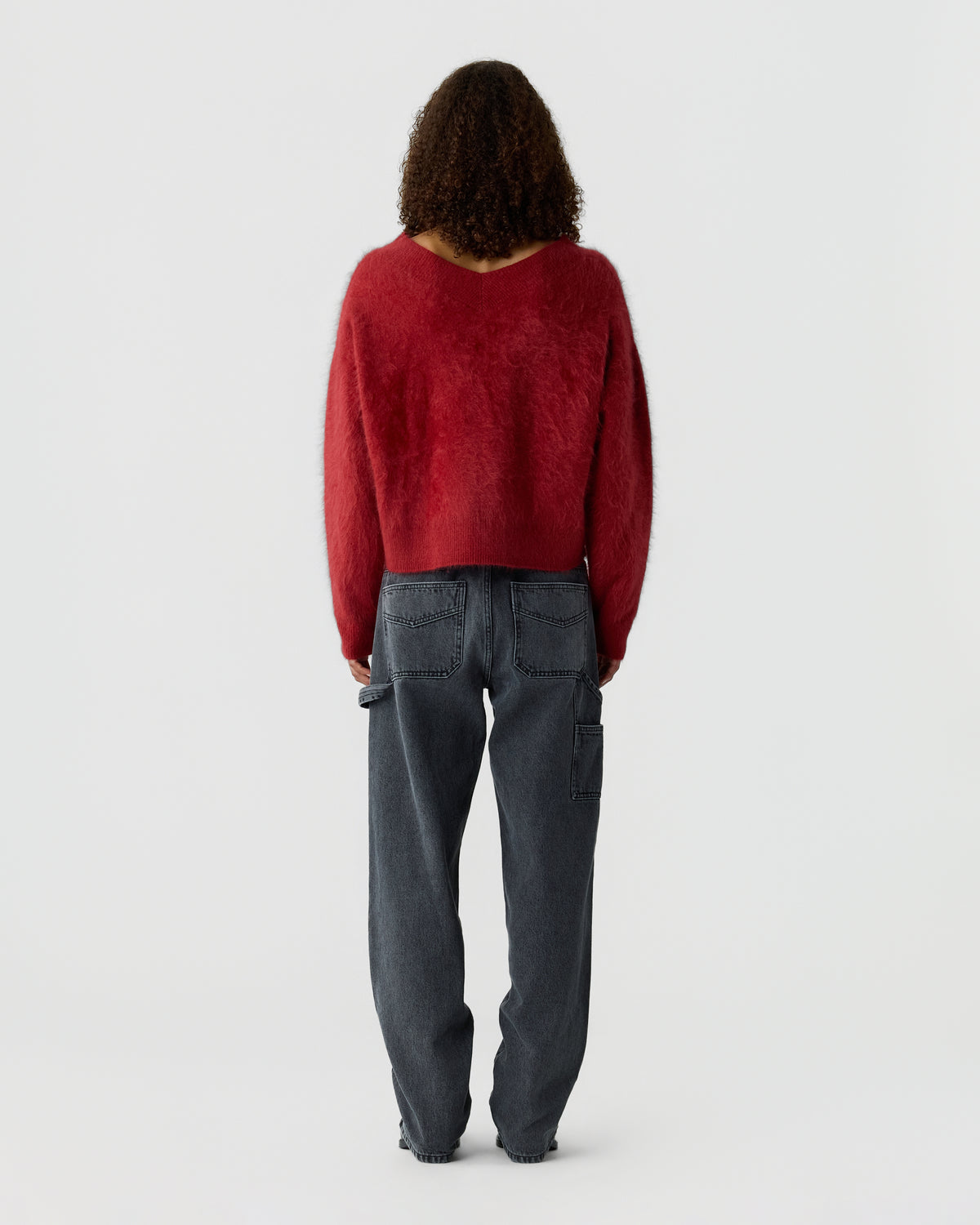 Person seen from behind wearing a deep red sweater and dark gray cargo pants against a plain light gray studio background