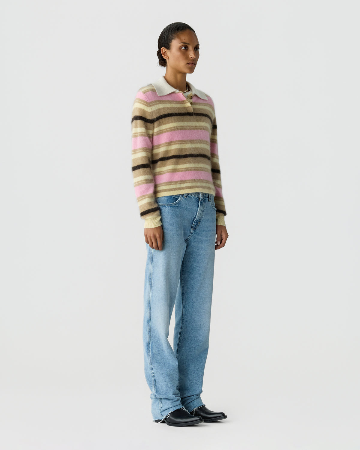 Woman wearing a striped collared sweater with blue wide-leg jeans and black shoes while standing against a light gray background