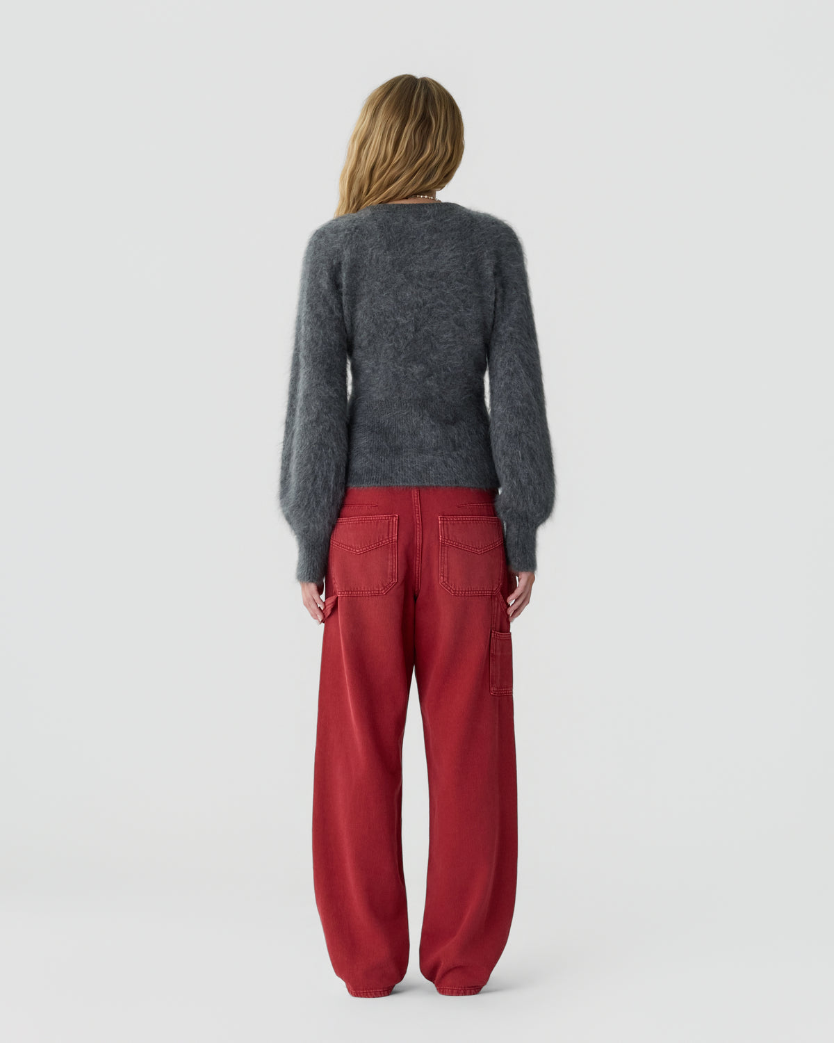 Person viewed from behind wearing a dark gray long sleeve sweater and loose red trousers against a plain light gray background