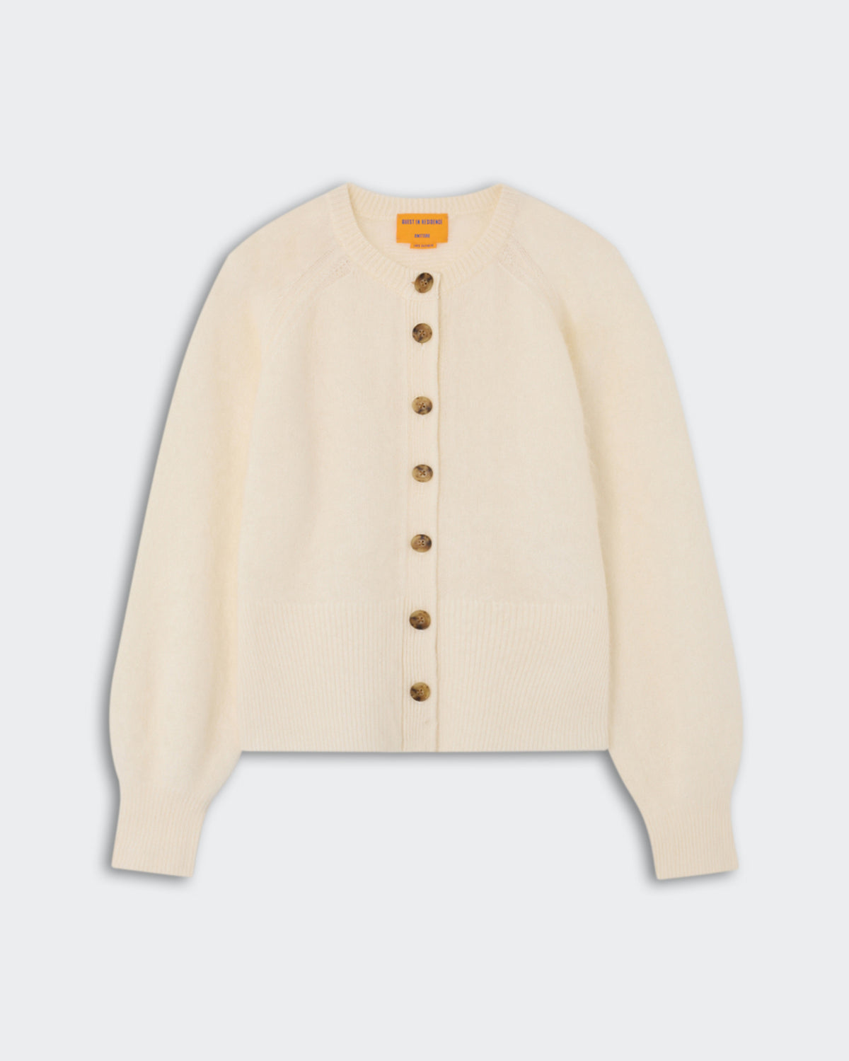 Cream-colored knit cardigan with seven tortoiseshell buttons down the front, long sleeves, and ribbed cuffs and hem, photographed on a light background.