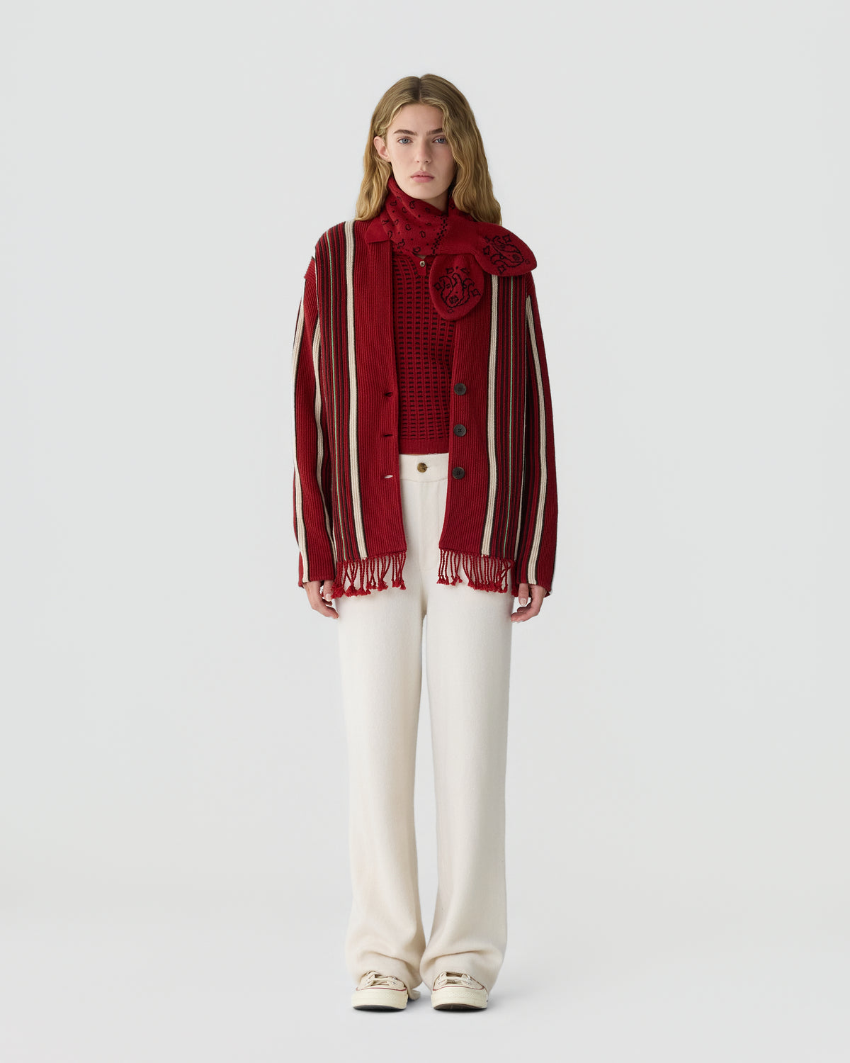 Woman wearing a red and white striped cardigan over a red patterned top with a matching red scarf and high-waisted white wide-leg pants against a plain background.