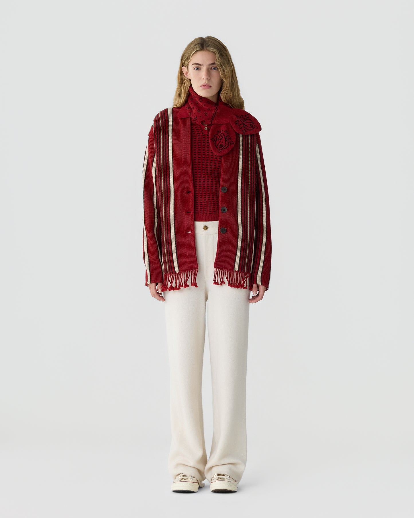 Woman wearing a red and white striped cardigan over a red patterned top with a matching red scarf and high-waisted white wide-leg pants against a plain background.