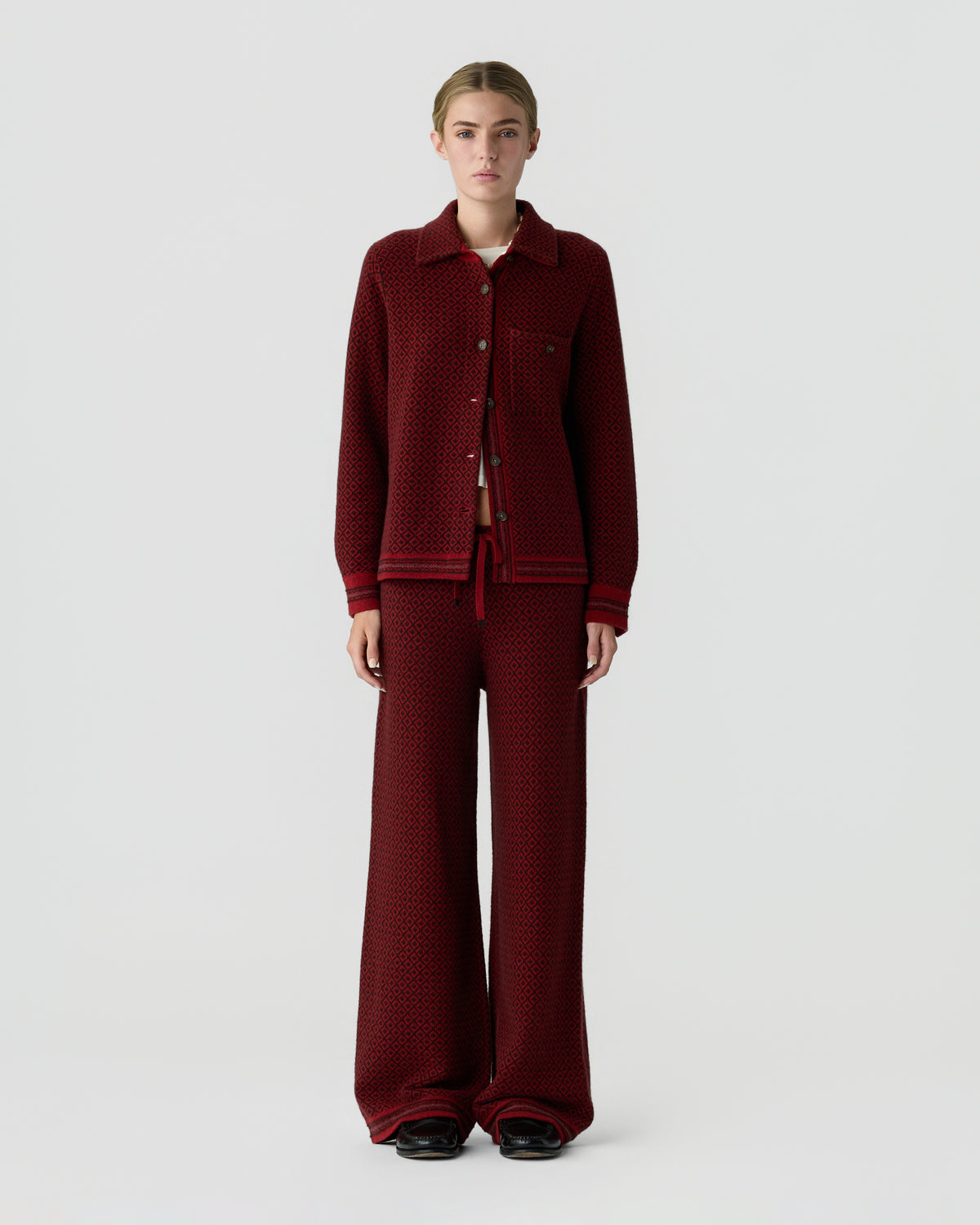 Person standing against a light gray background wearing a dark red button front cardigan with matching wide leg trousers and black shoes