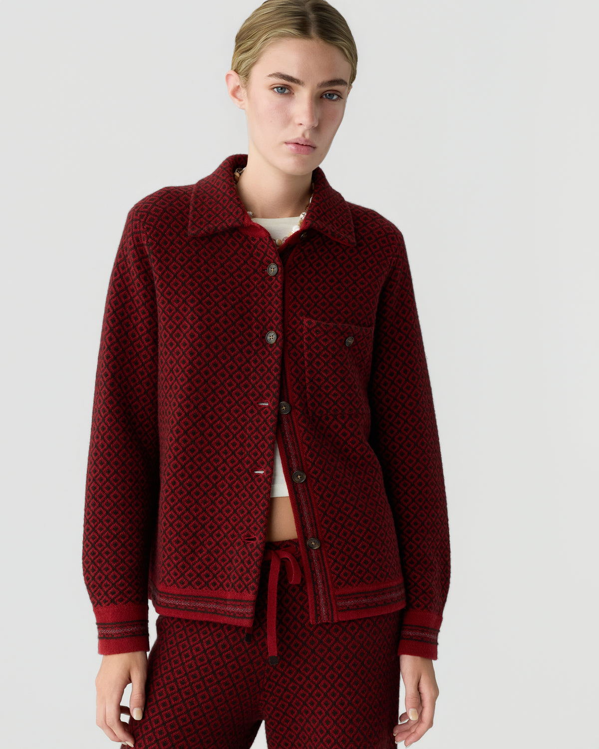 Model wearing a burgundy button front jacket with a geometric pattern and matching trousers against a light gray background