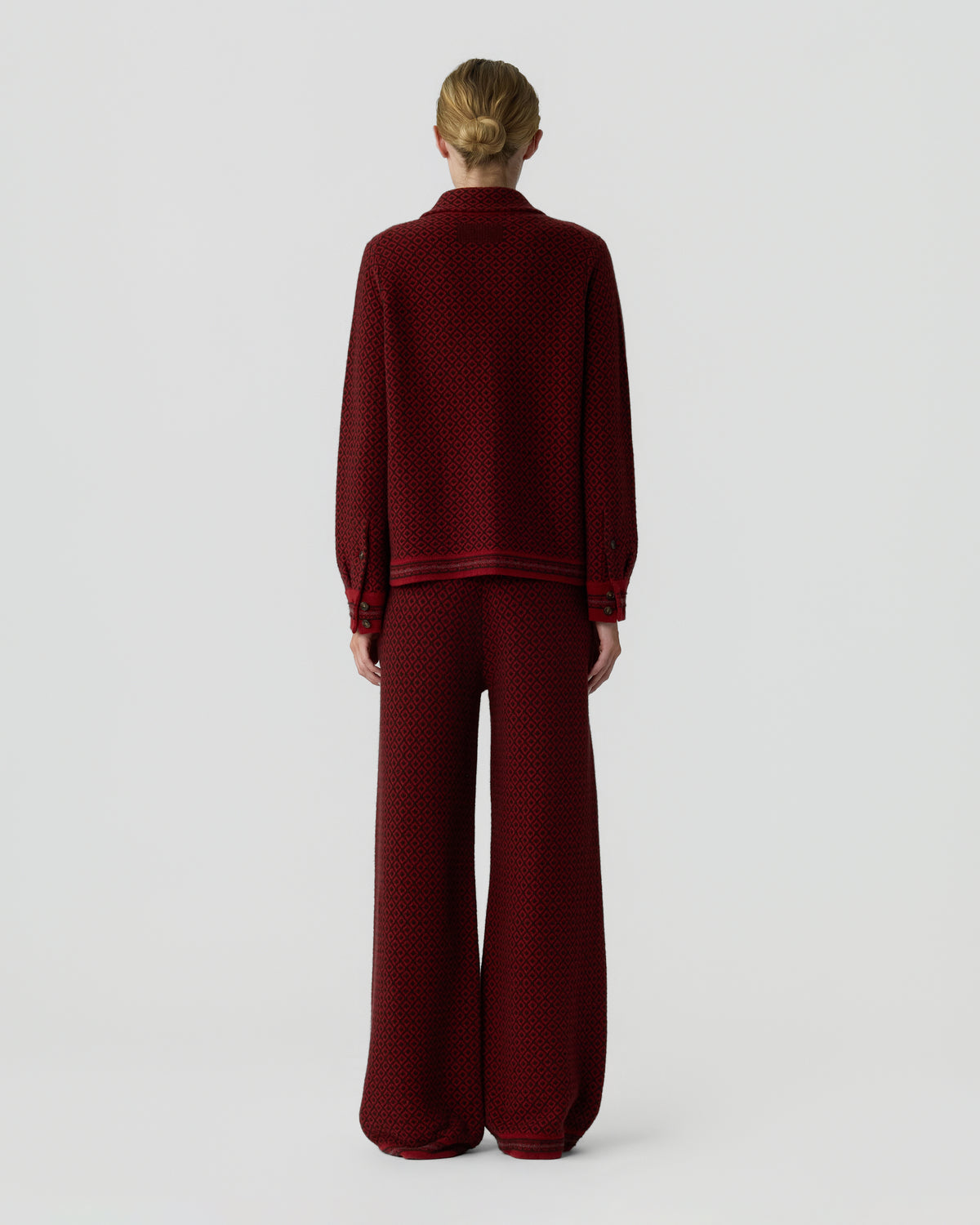 Model viewed from behind wearing a burgundy knitted sweater and matching wide leg pants against a light gray background