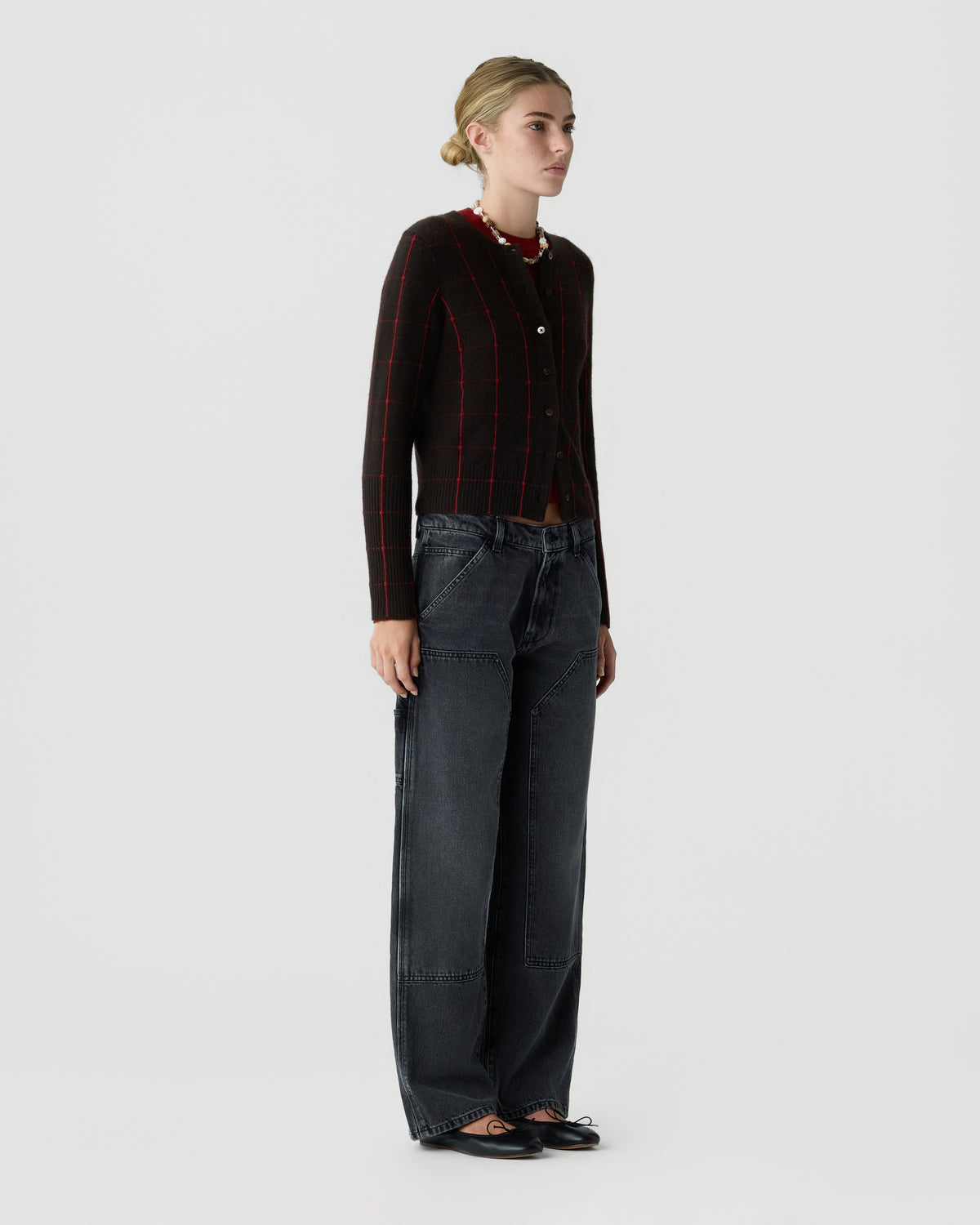 Model wearing a black cardigan with subtle red stripes, dark wide-leg jeans, and black flats against a light gray studio background