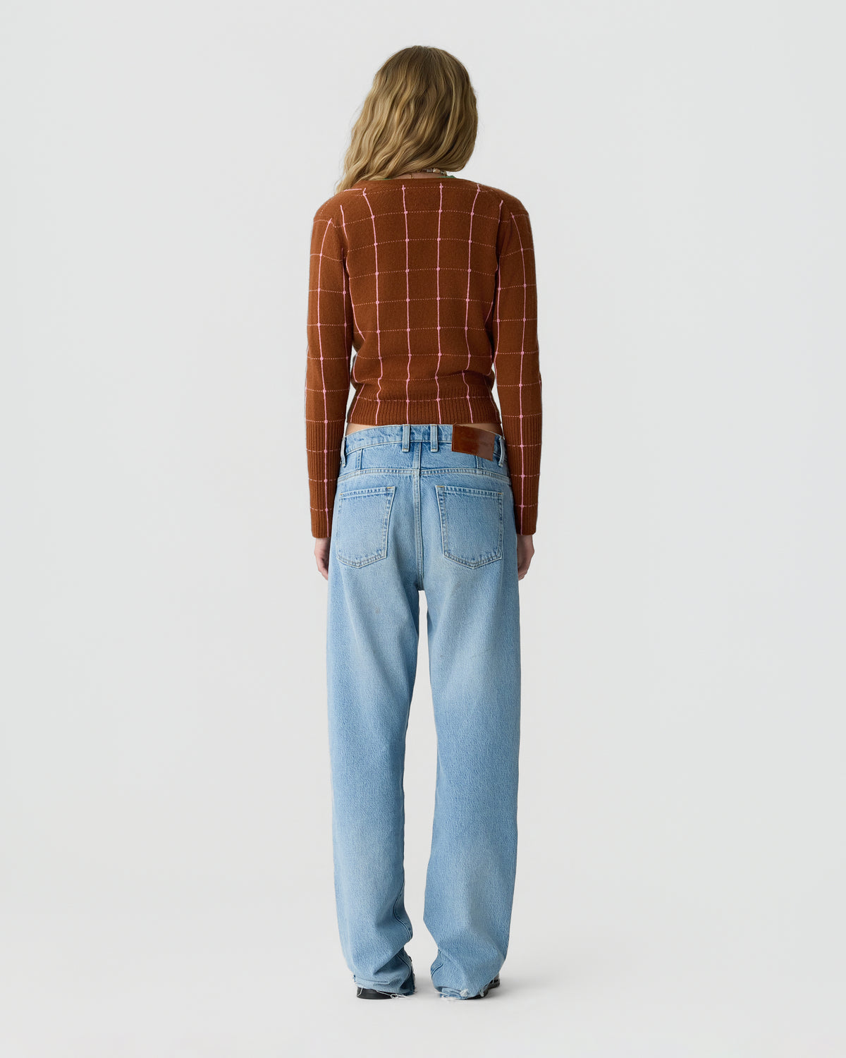 Back view of a person wearing a brown checked long sleeve top and relaxed light blue jeans against a plain light gray background