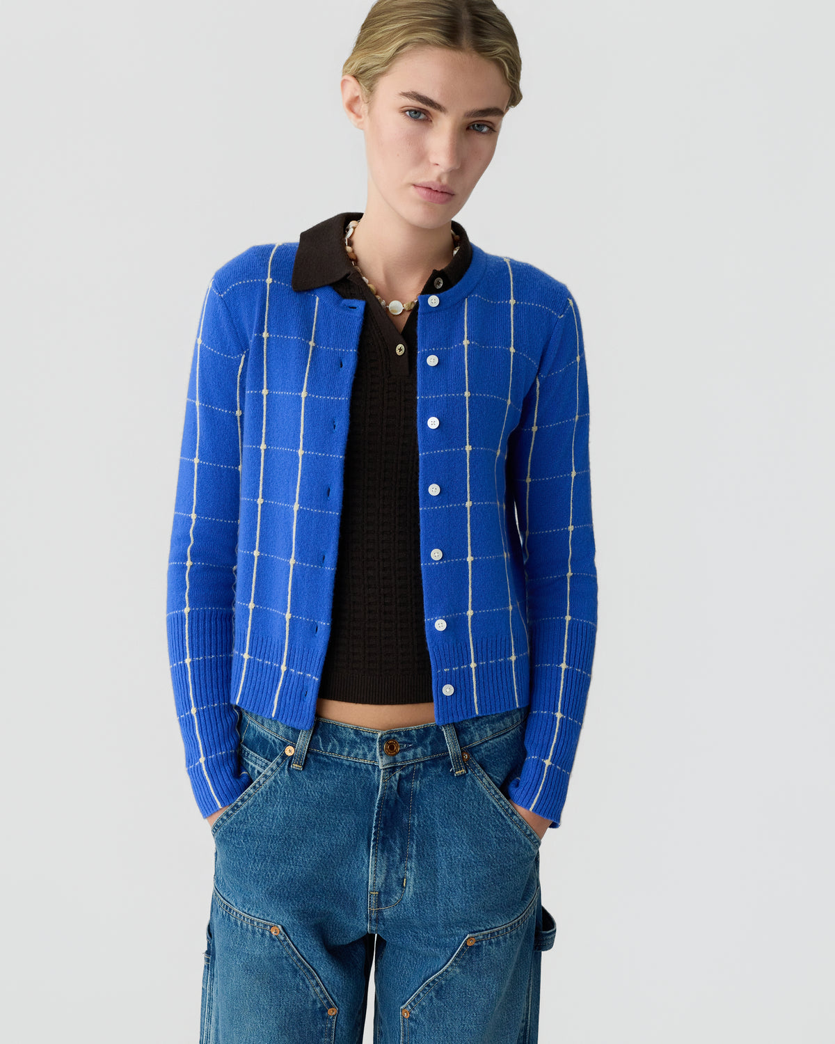 Model wearing a bright blue checked cardigan over a black collared top with relaxed blue jeans against a light gray background