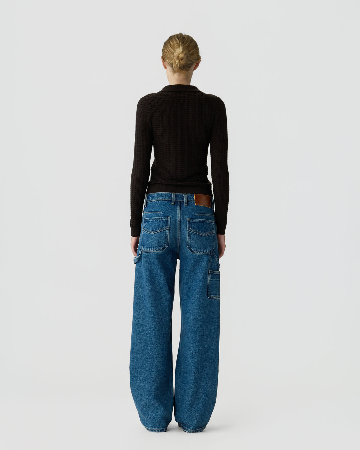 Person viewed from behind wearing a black long sleeve top and relaxed blue jeans against a light gray background