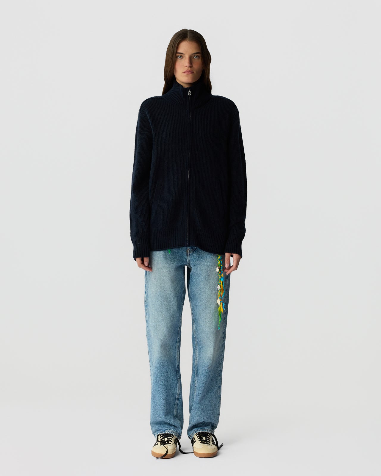 Person wearing a black sweater and light blue jeans with floral embroidery on a white background