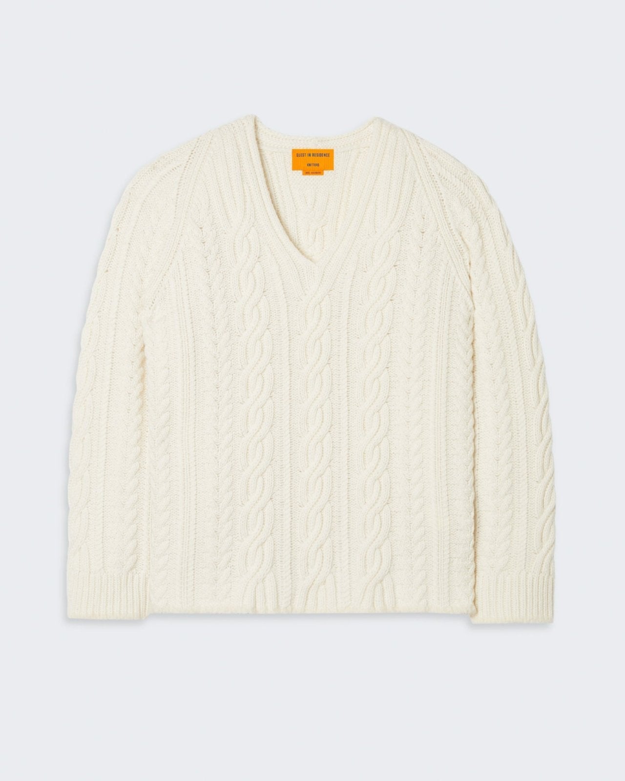 Cream-colored cable knit sweater with v-neck and relaxed, oversized fit.