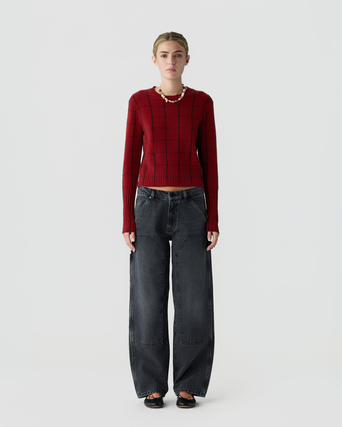 Model wearing a fitted red long sleeve sweater with dark wide leg jeans and black shoes against a light gray background