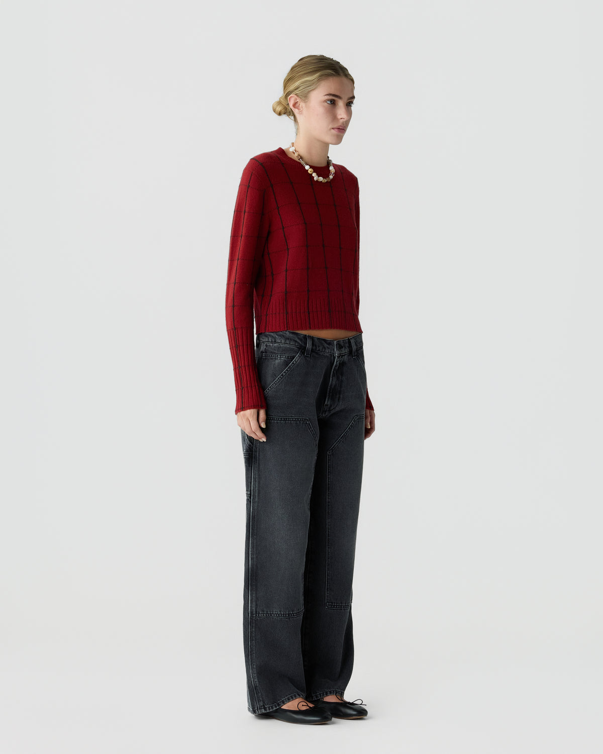 Model wearing a burgundy ribbed sweater with dark wide leg jeans and black shoes against a light gray studio background