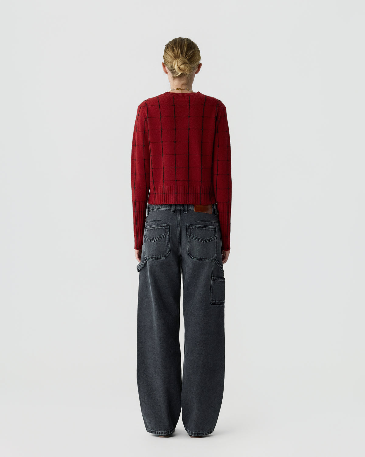 Back view of a person wearing a red checkered sweater with a cropped hem and relaxed dark gray cargo jeans against a light gray background