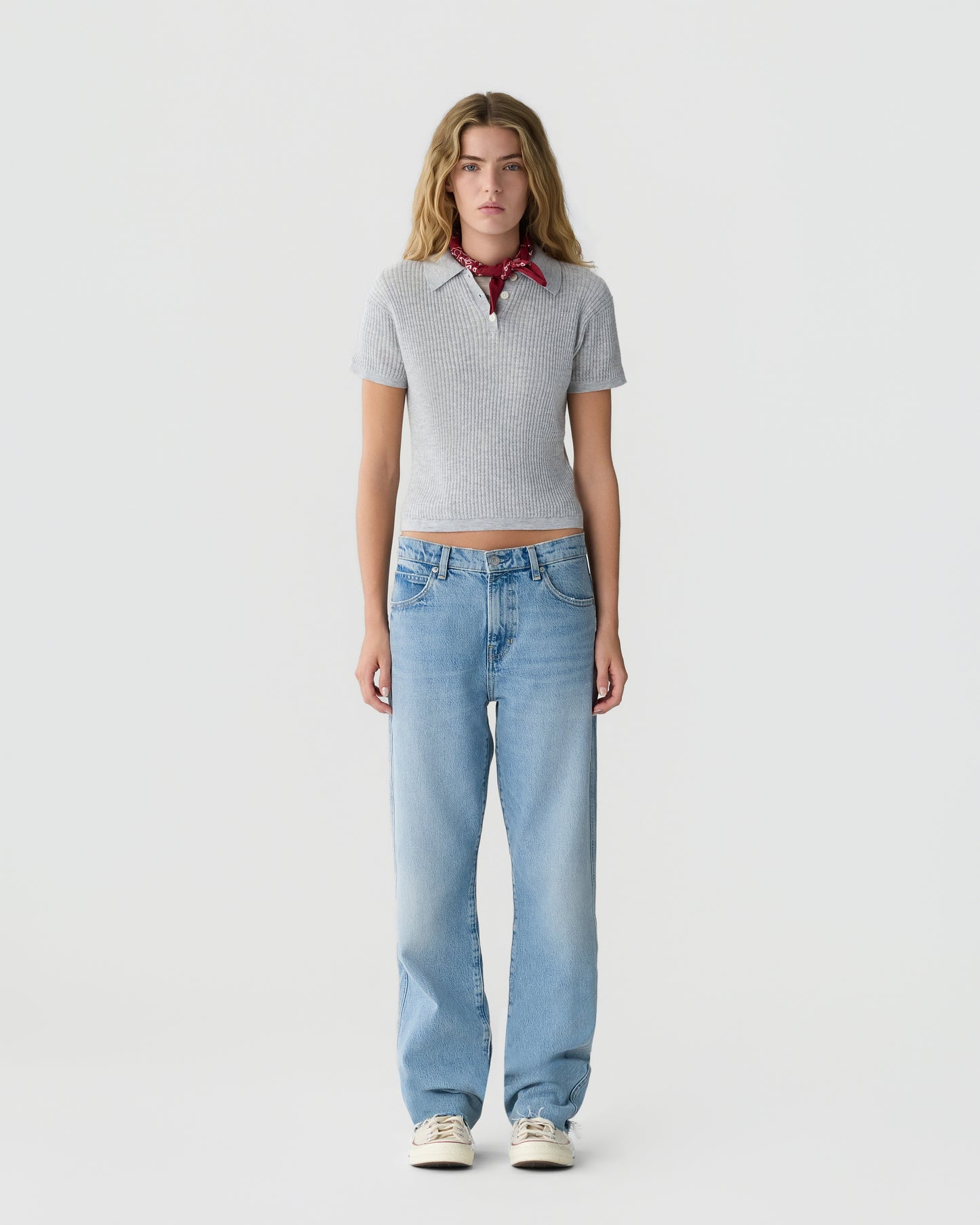 Model wearing a gray ribbed short sleeve top with a red neck scarf light blue jeans and cream sneakers against a plain light gray background