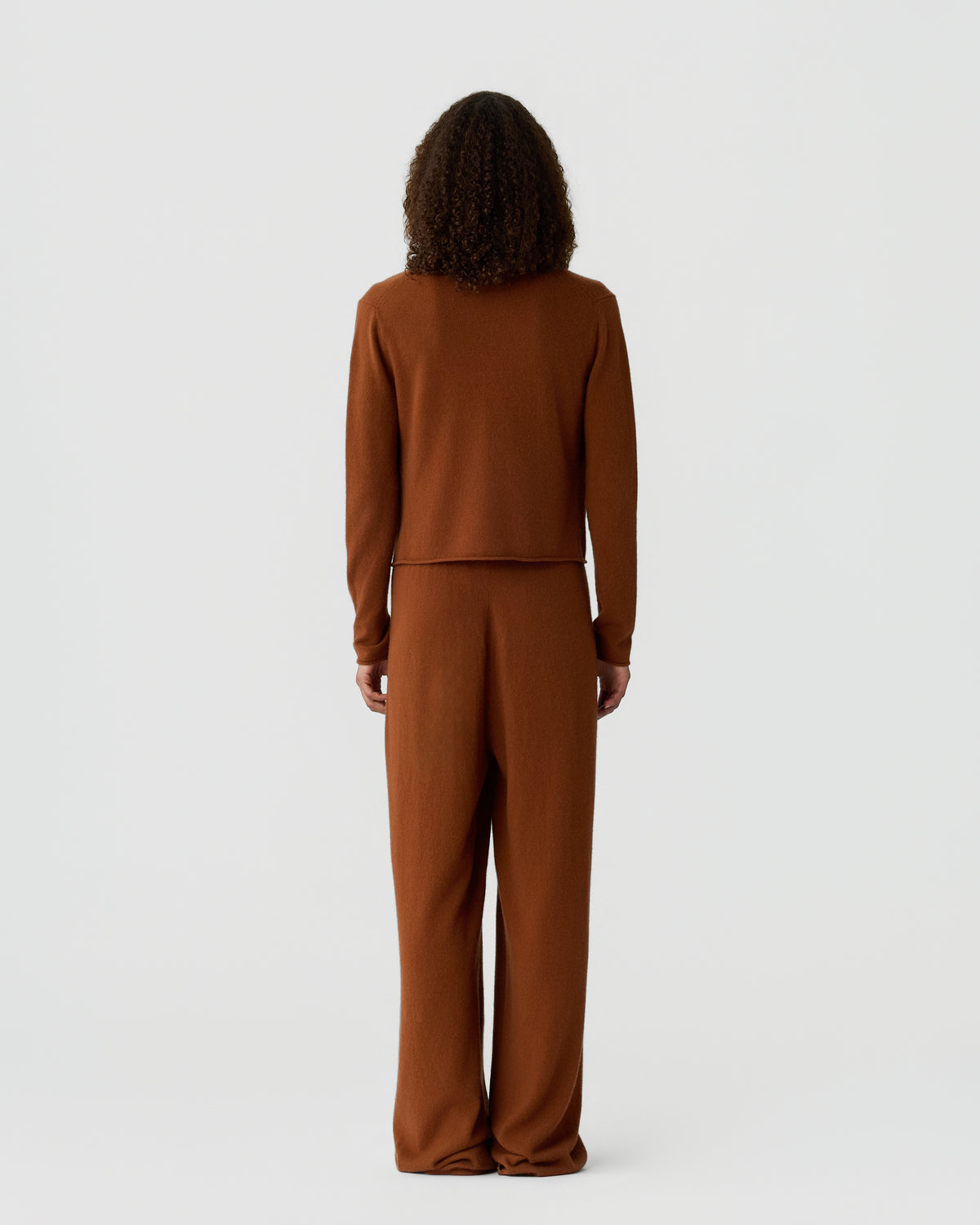 Model shown from behind wearing a brown long sleeve knit top and matching wide leg trousers against a light gray background