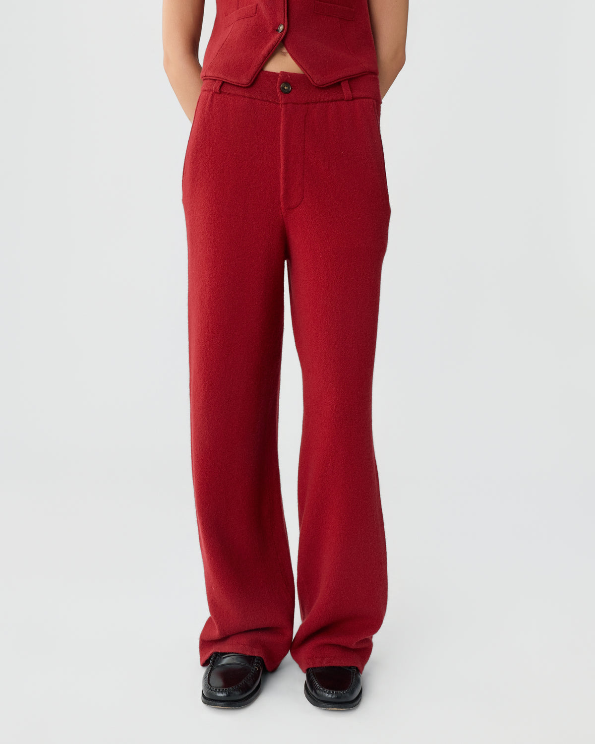 Lower half of a person wearing red wide-leg pants and black shoes, with part of a matching red vest visible against a plain white background.