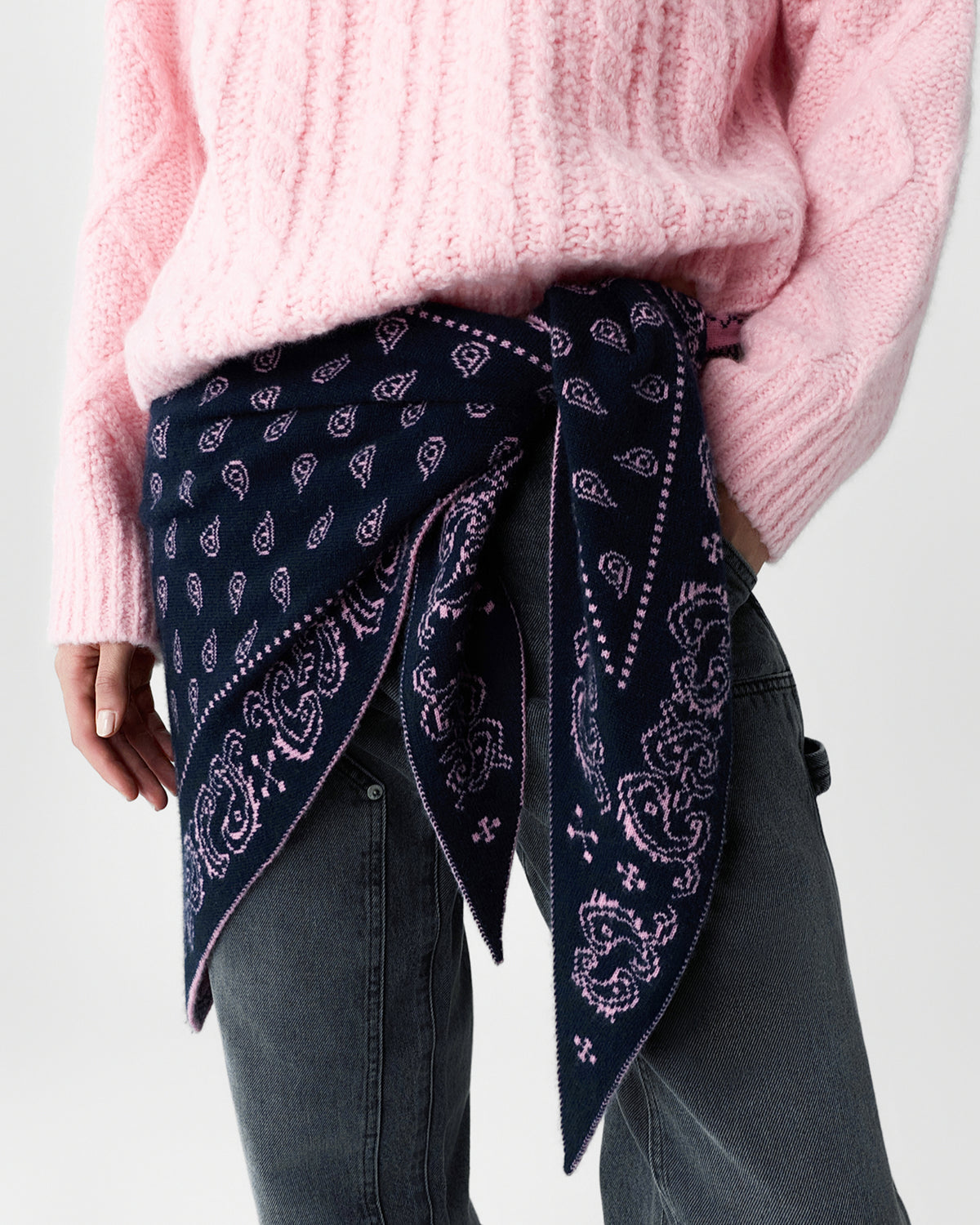 Cropped view of a person wearing a soft pink sweater and dark gray jeans with a navy paisley scarf tied around the waist