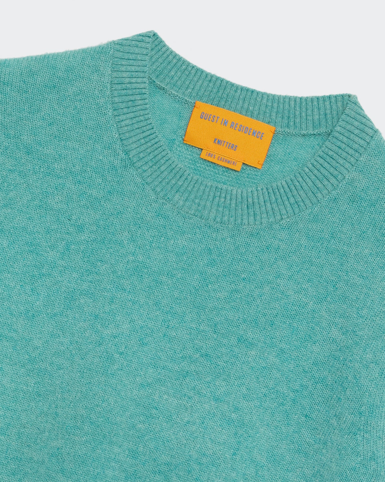 Shrunken Crew - Glacier teal knitted crewneck sweater with ribbed collar and orange brand label on light background