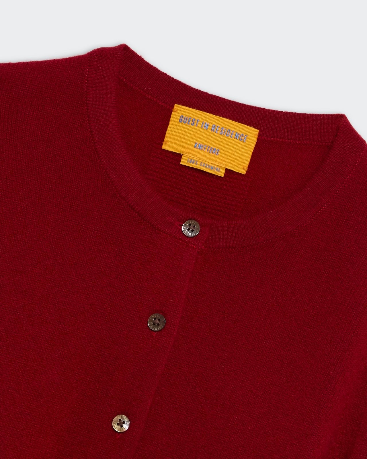 Jane Cardigan - Ruby close-up of red knit fabric with round neckline and three dark buttons fastened